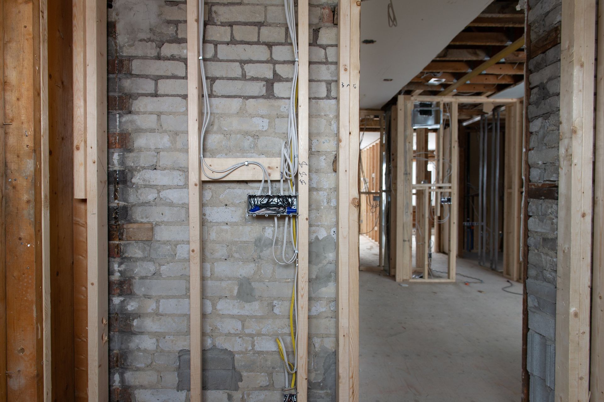 Electrical wires connected into a metal box in a residential renovation site in Ontario, Canada. The wires are stapled to the wooden studs. A brick wall is visible in background.